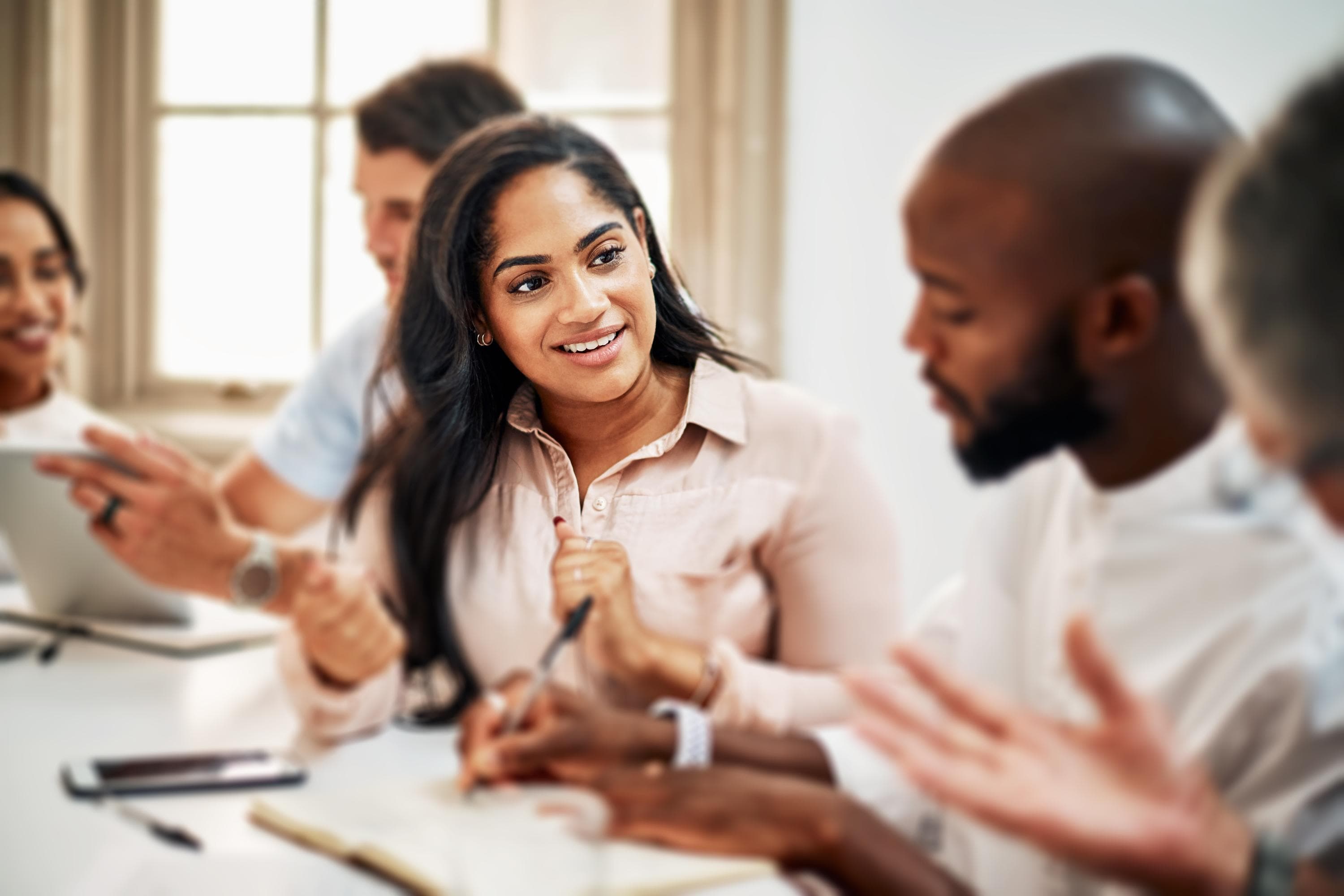 A group of colleagues engages in a lively discussion around a table in a well-lit room, illustrating collaboration and exchange of ideas.