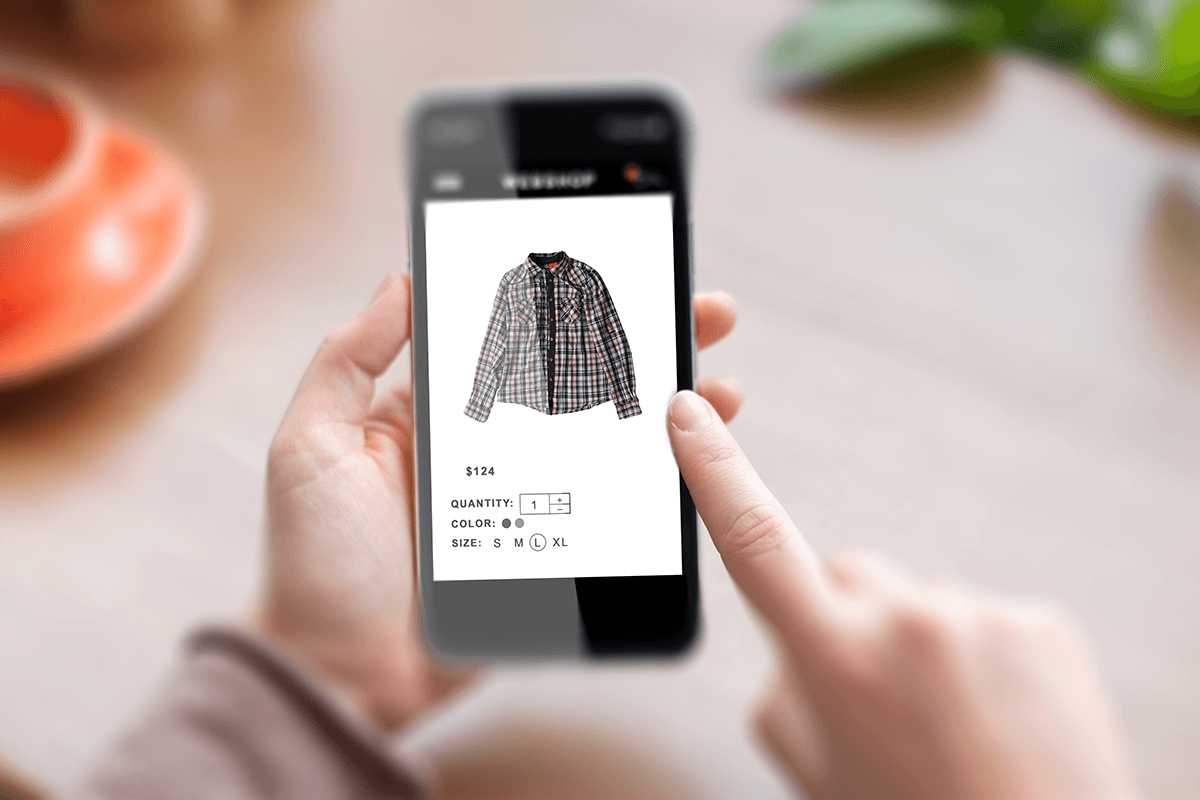 A person's hand holding a smartphone, displaying a shopping app with a product page for a plaid shirt.