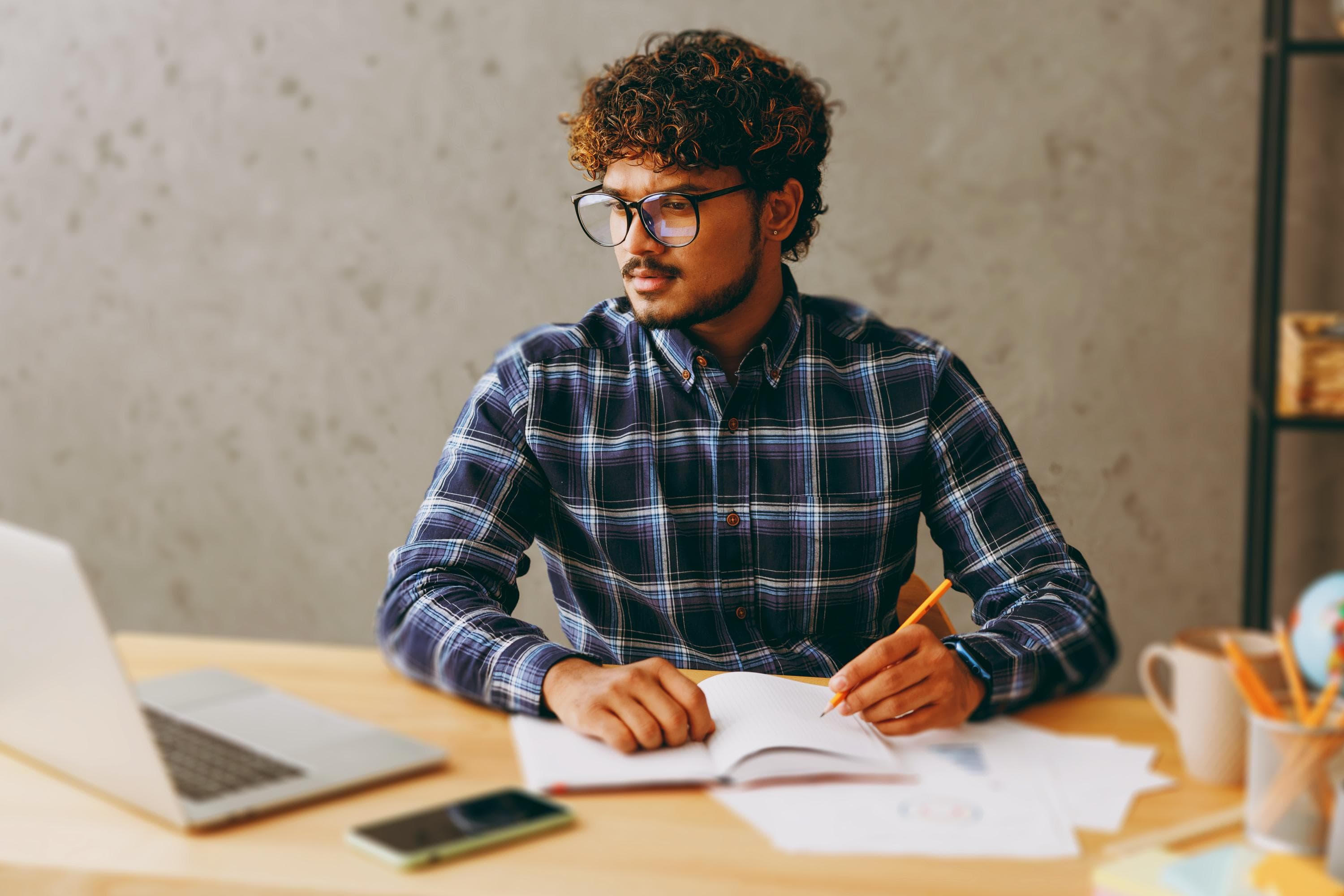 A person with curly hair is focused on studying at a desk, surrounded by books, a laptop and a coffee mug, emphasizing a moment of concentration and learning.