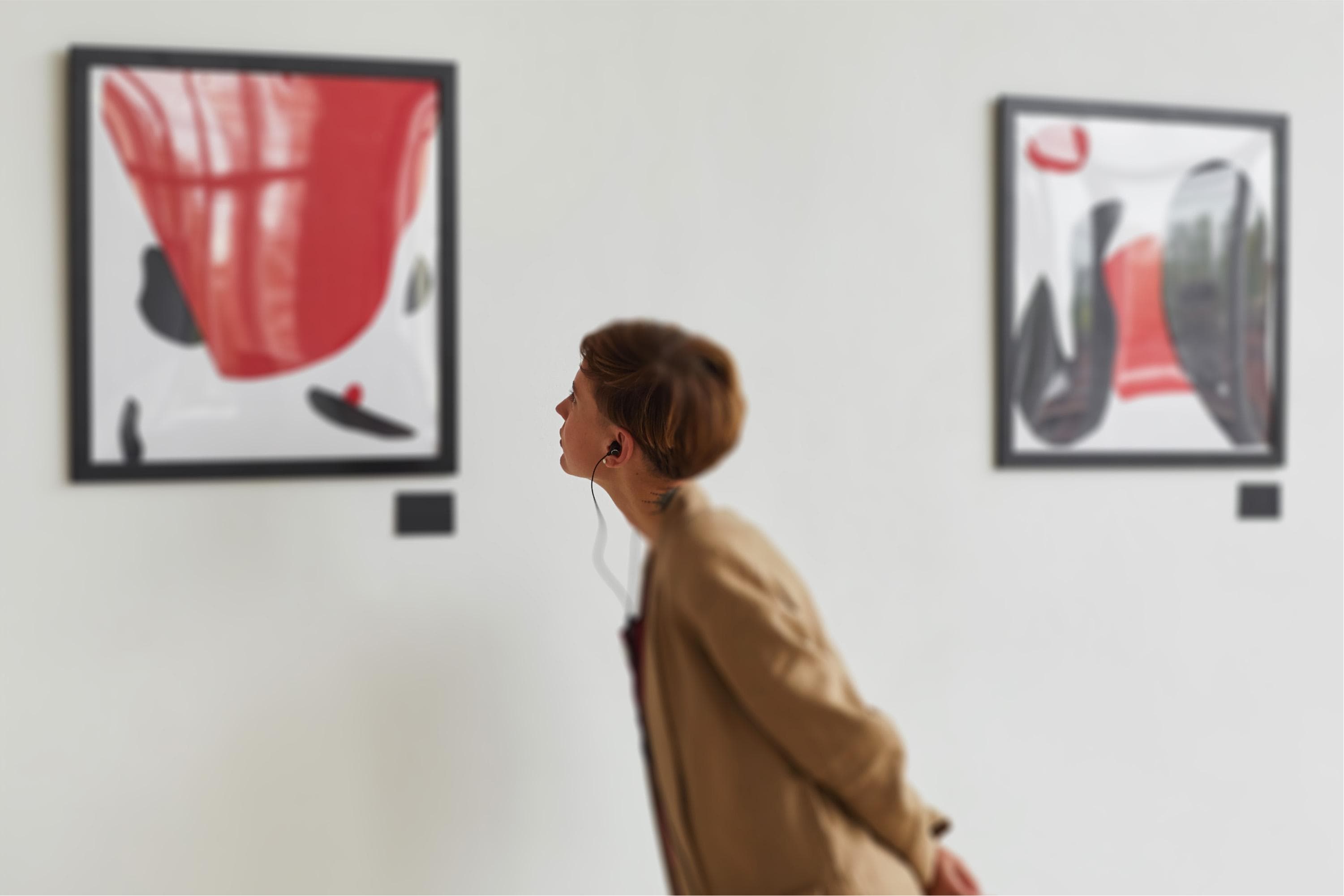 A person in a gallery observing a modern art piece. They stand profiled, intently looking at a framed artwork of abstract designs, dressed in a casual trench coat.