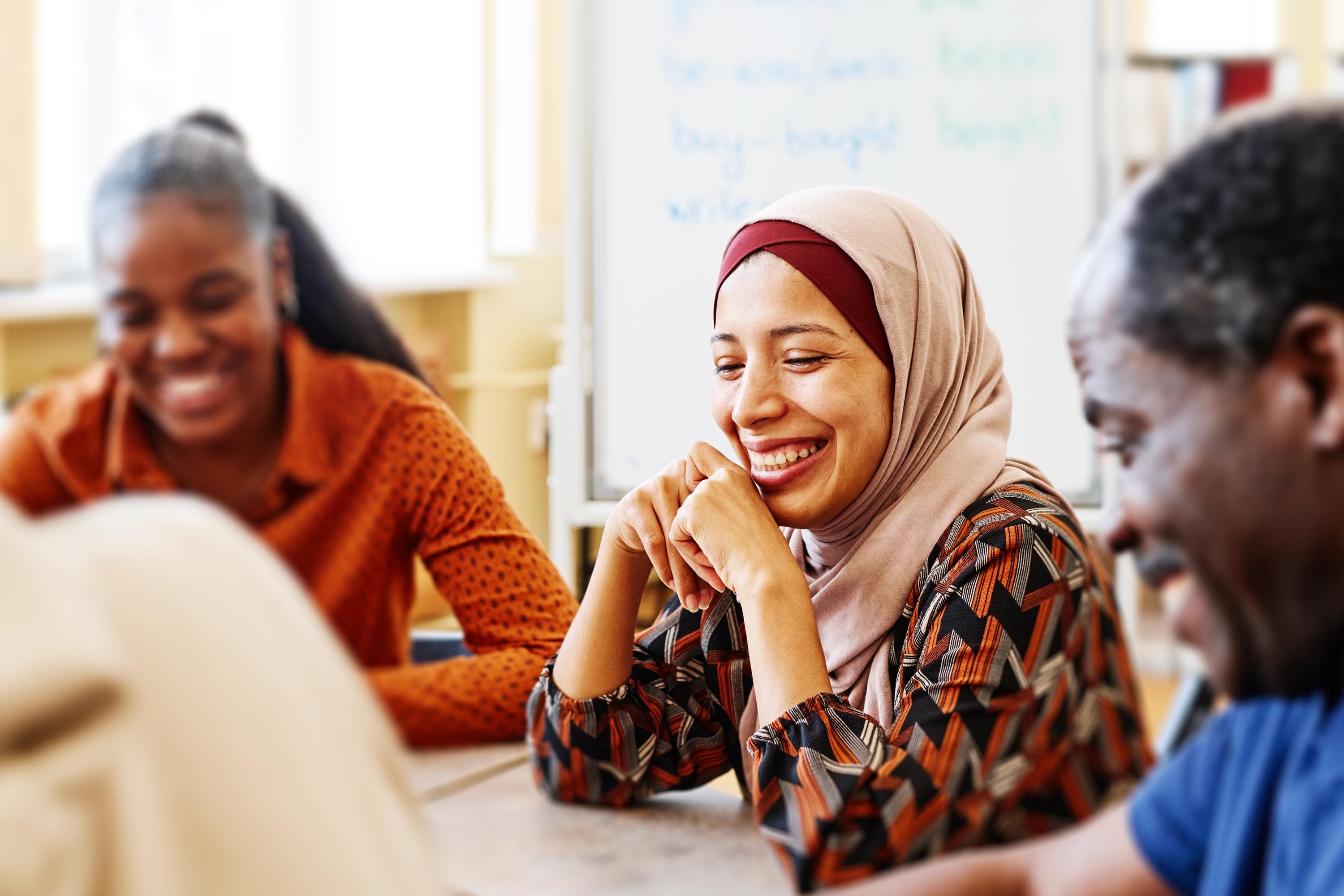 A diverse group of individuals shares a light-hearted moment during a workshop, with smiles and engagement that convey a sense of community and learning together.